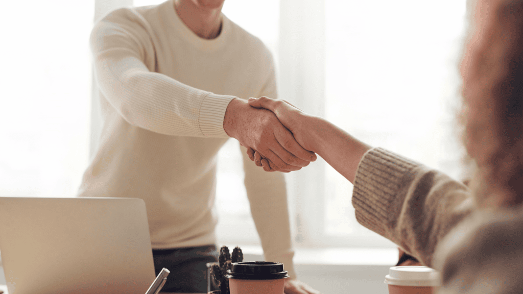Two people shaking hands across a desk in a business meeting or agreement setting.