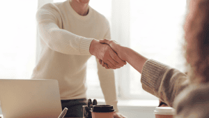 Two people shaking hands across a desk in a business meeting or agreement setting.
