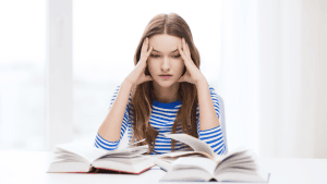 A person holding their head in their hands while looking at books